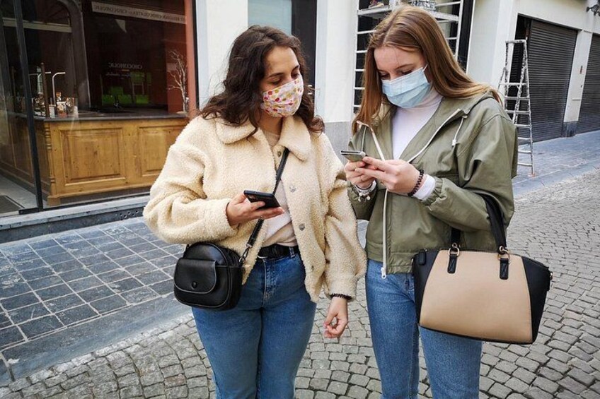 Two people standing on a cobblestone street, one holding a phone and the other looking at it. 3