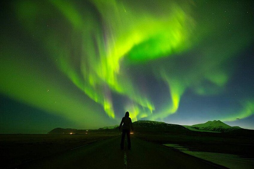 Una persona parada en una carretera con la aurora boreal al fondo. 4