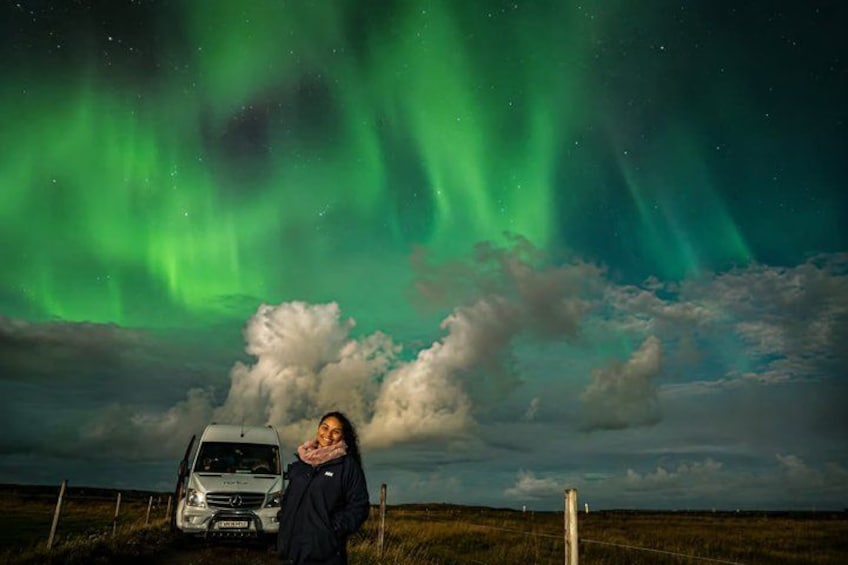 Una persona de pie junto a un vehículo bajo un cielo con aurora boreal verde. 1
