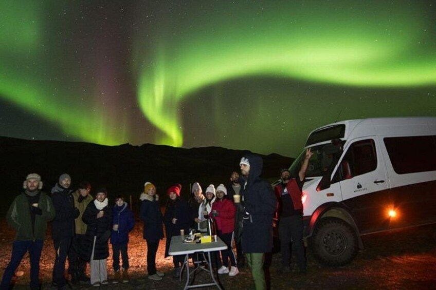 Un grupo de personas de pie frente a un vehículo bajo un cielo nocturno con auroras boreales. 3