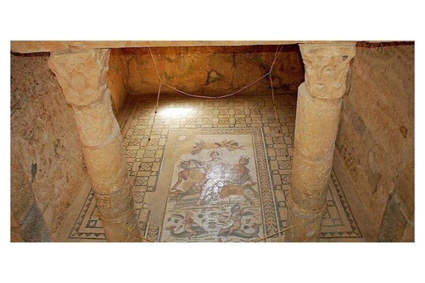 Une ancienne mosaïque située sous des colonnes de pierre, ornée de motifs géométriques et présentant une figure centrale. 3