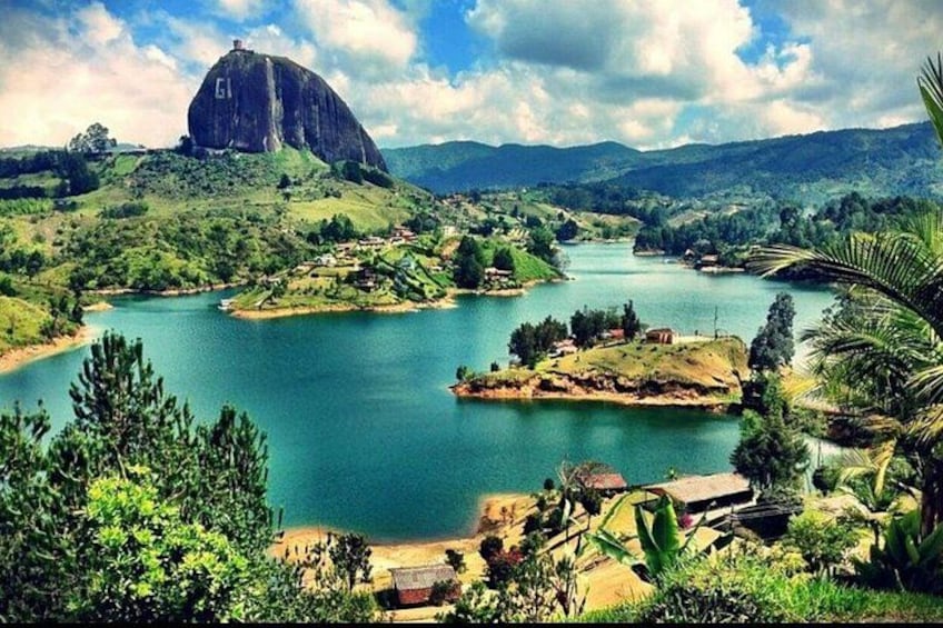 A river winding through a lush landscape with a prominent rock formation and scattered buildings. 3