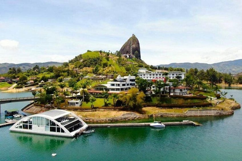 A river with a boat docked, a large hill with a distinctive peak, and several buildings on the riverbank. 5