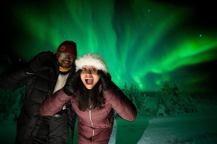 Dos personas vestidas para el invierno, un paisaje nevado y la aurora boreal. 1