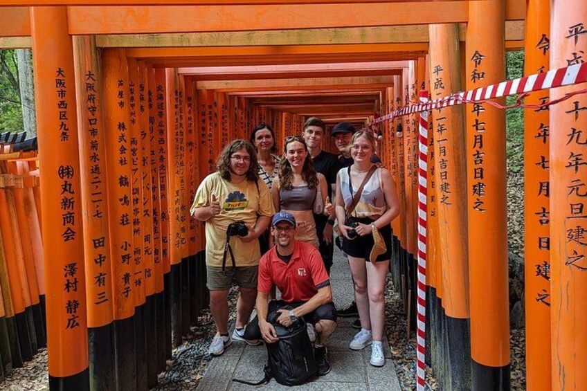 A group of people standing in front of a row of orange torii gates with Japanese inscriptions. 1