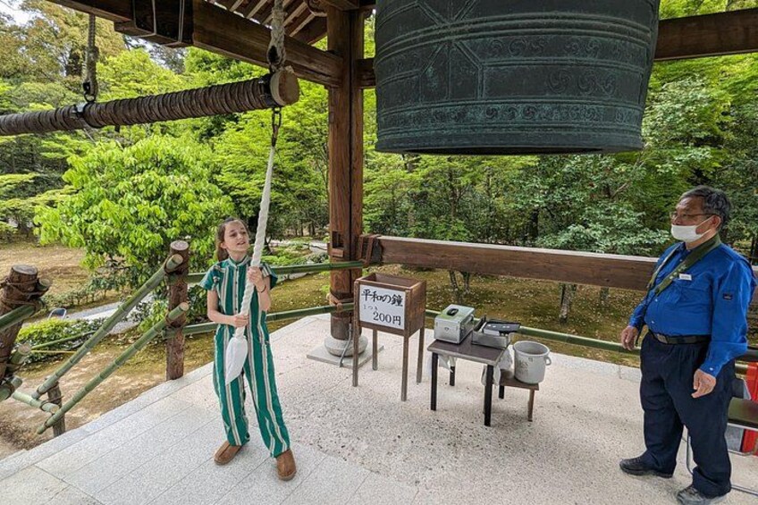A person in a green and white striped dress swinging on a rope, a large bell hanging from a wooden structure, and a sign with Japanese characters. 3