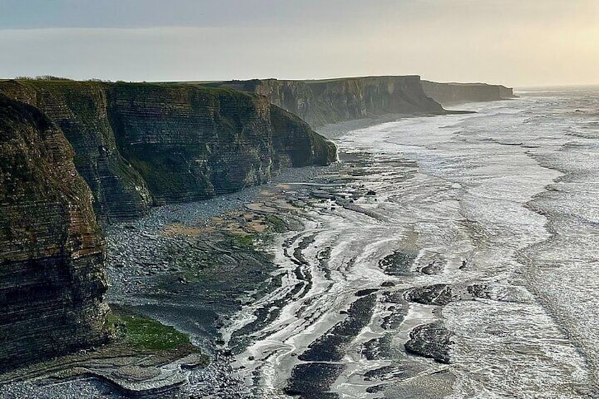 A coastal cliff with layered rock formations and a turbulent sea. 4