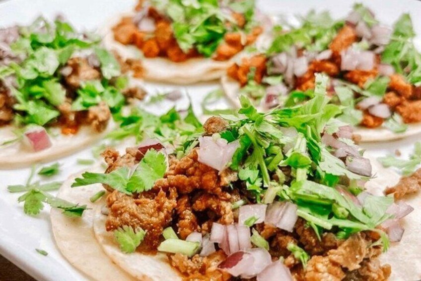 A plate of tacos topped with meat, onions, and cilantro. 4
