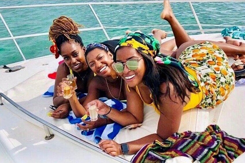 Tres personas en un bote, vestidas con trajes de baño de colores, sosteniendo bebidas en sus manos. 3