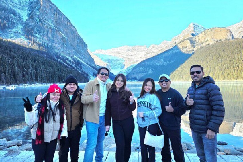 A group of people standing by a lake with mountains in the background. 2