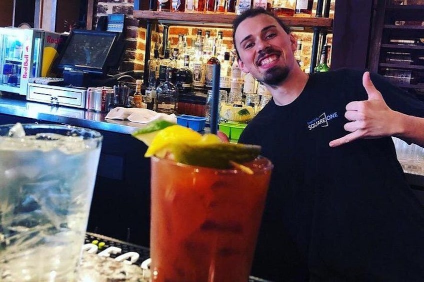 A bar with a bartender, a glass of red drink with a lime garnish, and a Red Bull refrigerator. 4