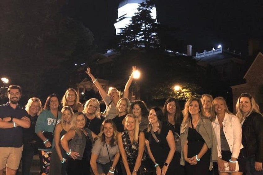 A group of people outdoors at night with a building and a tower in the background. 1