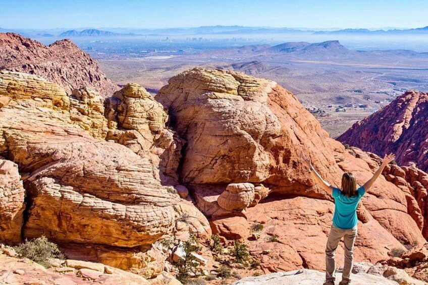 Una persona de pie sobre un afloramiento rocoso con los brazos levantados, contemplando un extenso paisaje desértico con montañas lejanas. 5