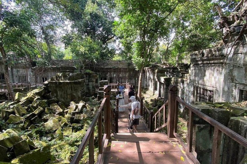 A stone pathway leading through a lush, green forested area with ancient stone structures and a wooden railing. 4