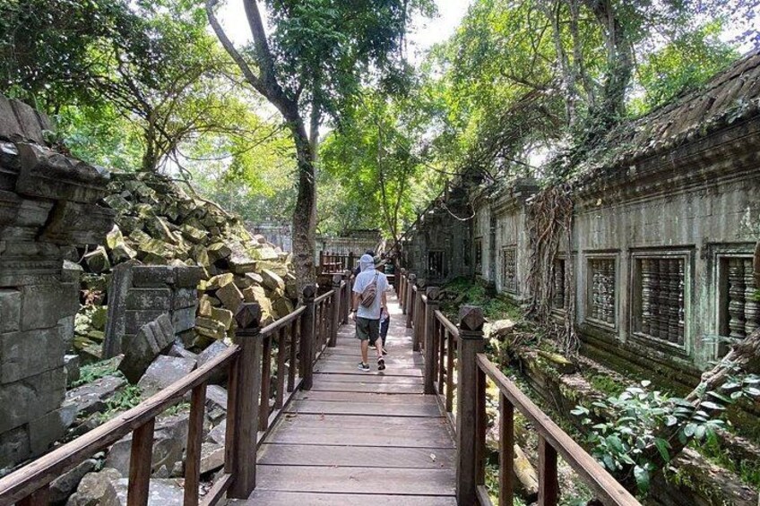 A wooden pathway flanked by stone walls and vegetation, leading through a lush, green area. 5