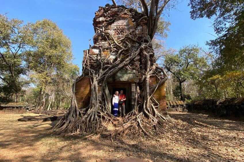 Un arbre aux racines tentaculaires qui s'enroulent autour d'une structure délabrée, peut-être un temple, et où se tient une personne à l'intérieur. 4