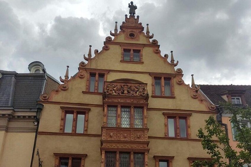 A historic building with ornate architectural details, including a central balcony and a statue on top. 3