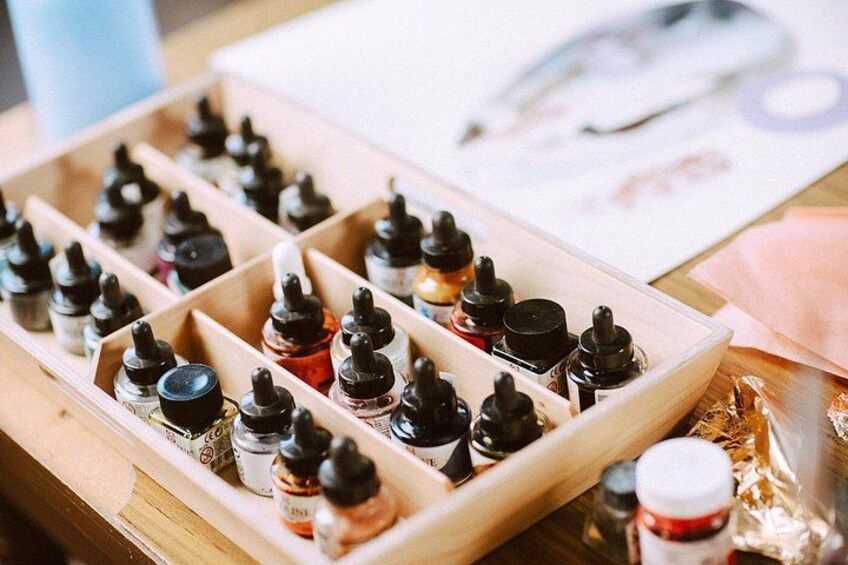 A wooden tray with multiple bottles of ink, some with black caps and others with red caps, on a wooden surface. 5