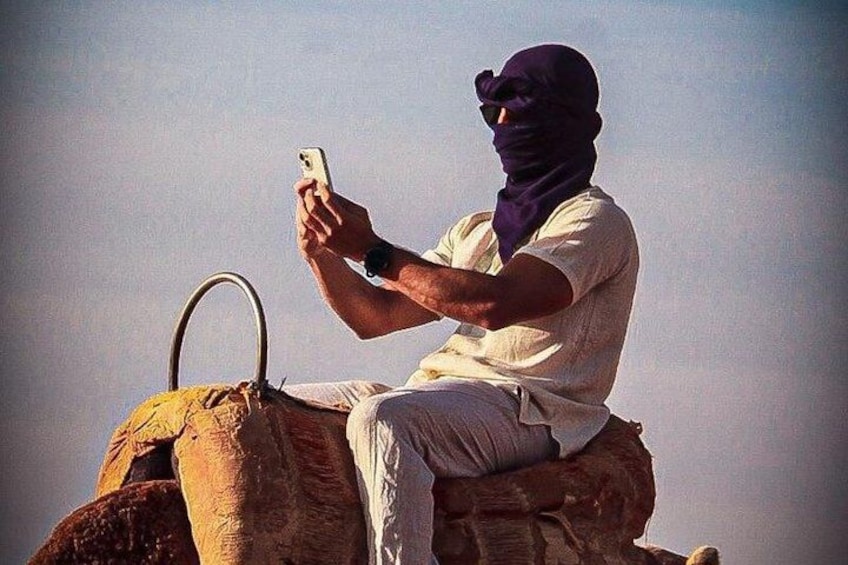 A person sitting on a camel, holding a smartphone. 1