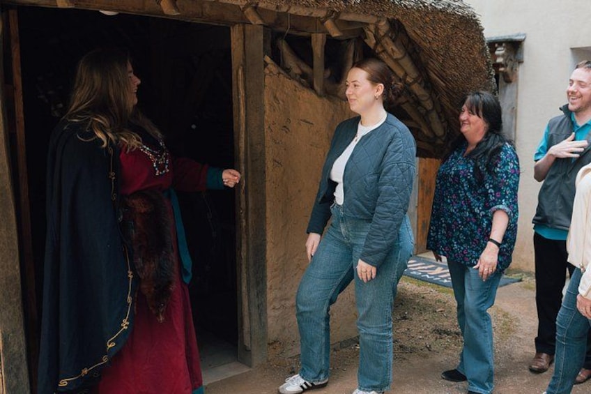 A group of people standing outside a rustic building with a thatched roof. 2