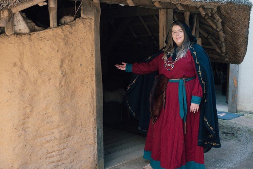 A person in traditional attire standing in front of a rustic building with a thatched roof. 5