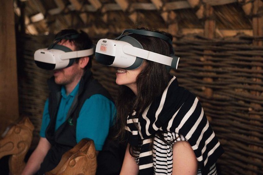 Two people wearing VR headsets in a rustic setting with wooden walls. 3