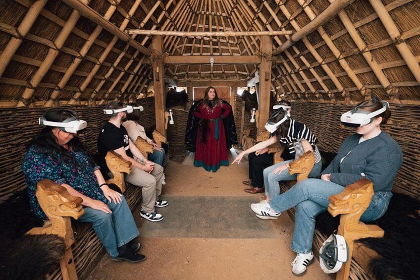 A group of people wearing VR headsets seated in a thatched-roof structure. 4