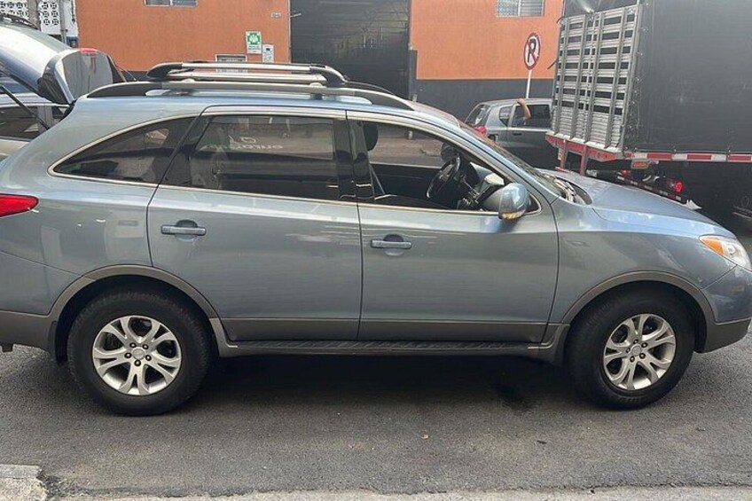 A silver hatchback parked on a street with buildings and a parking sign in the background. 2