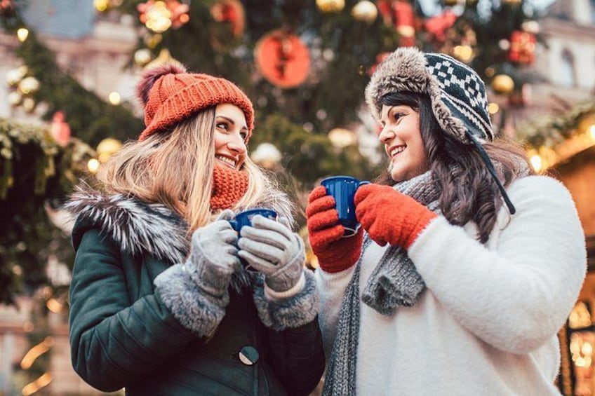 Two people holding cups, standing in front of a decorated Christmas tree. 3