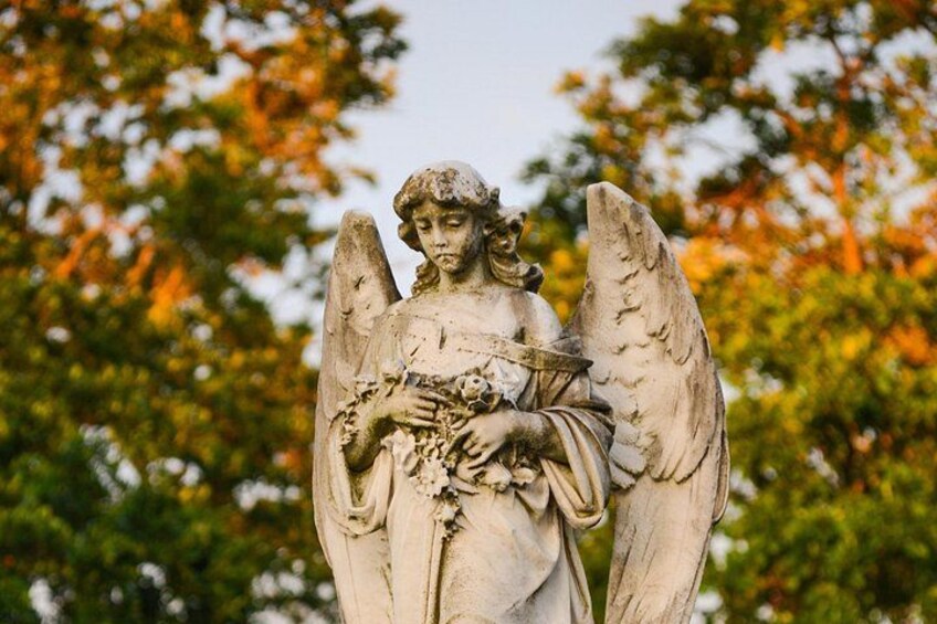 A statue of an angel with wings, set against a backdrop of autumn-colored trees. 3