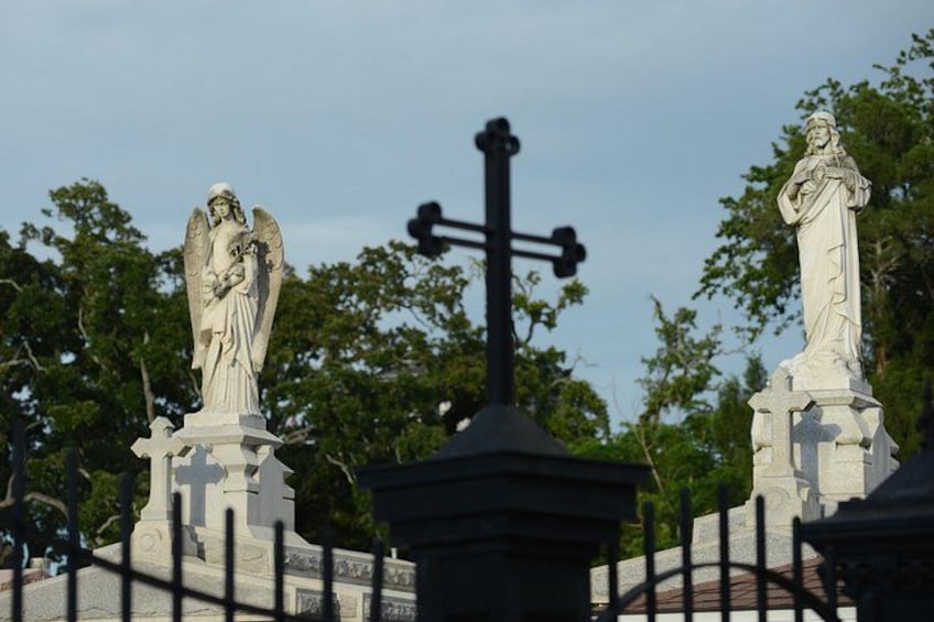 Un cementerio con dos estatuas, una de un ángel y otra de un santo, y una cruz al fondo. 5