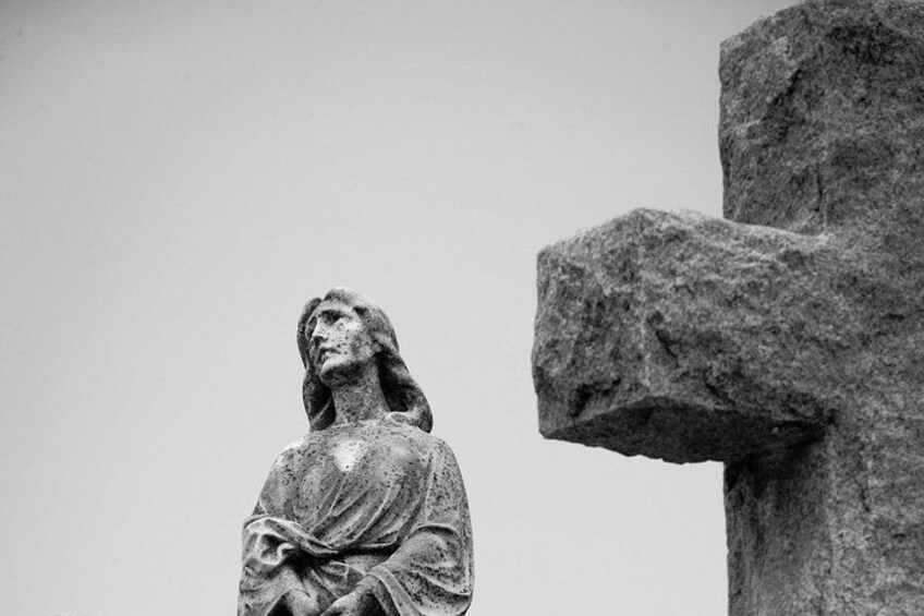 Una estatua de piedra de una mujer con una cruz al fondo. 3