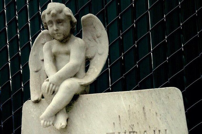 Una estatua de ángel de piedra con alas, sentada sobre un pedestal frente a una cerca de metal. 2