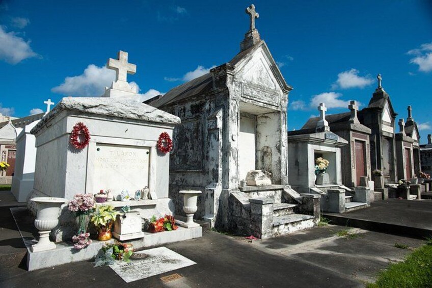 A cemetery with white headstones, some adorned with wreaths, under a clear blue sky. 4