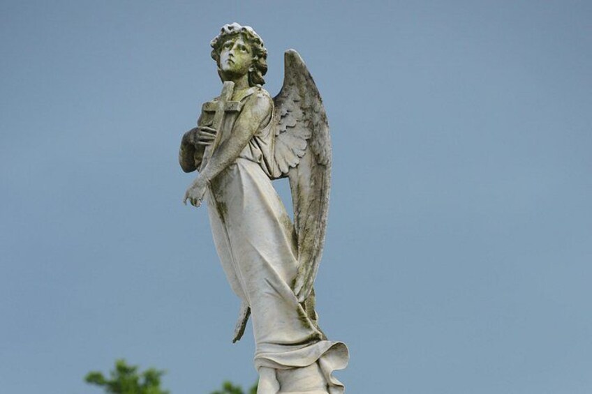 A statue of an angel with wings, holding a book, against a clear sky. 2
