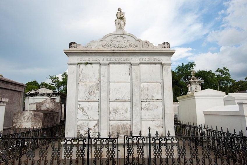 Un monumento de mármol blanco con una estatua en la parte superior, rodeado por una cerca de hierro forjado. 3