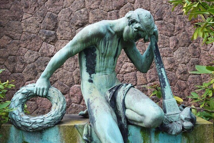 En staty som föreställer en man som håller i ett rep och en spade, placerad framför en stenmur. 1