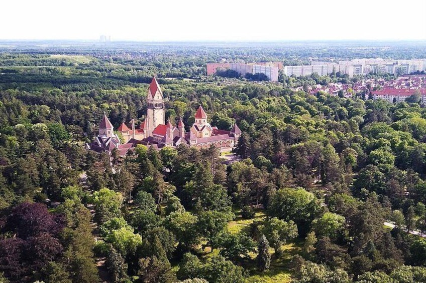 Eine Burg, umgeben von dichtem Wald, mit modernen Gebäuden im Hintergrund. 3