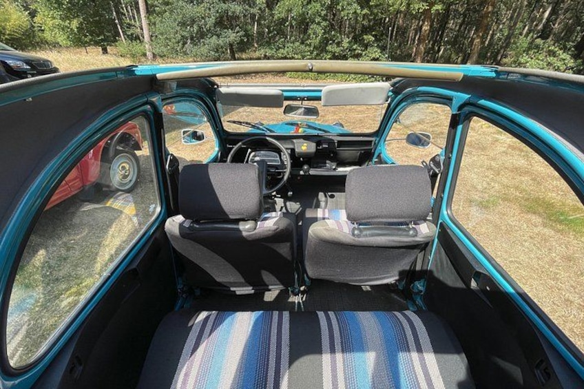 The interior of a vintage car with a teal exterior, two front seats, a steering wheel, and a dashboard. 5