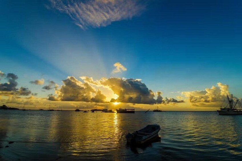 A sunset over a calm sea with a boat in the foreground and ships in the distance. 1
