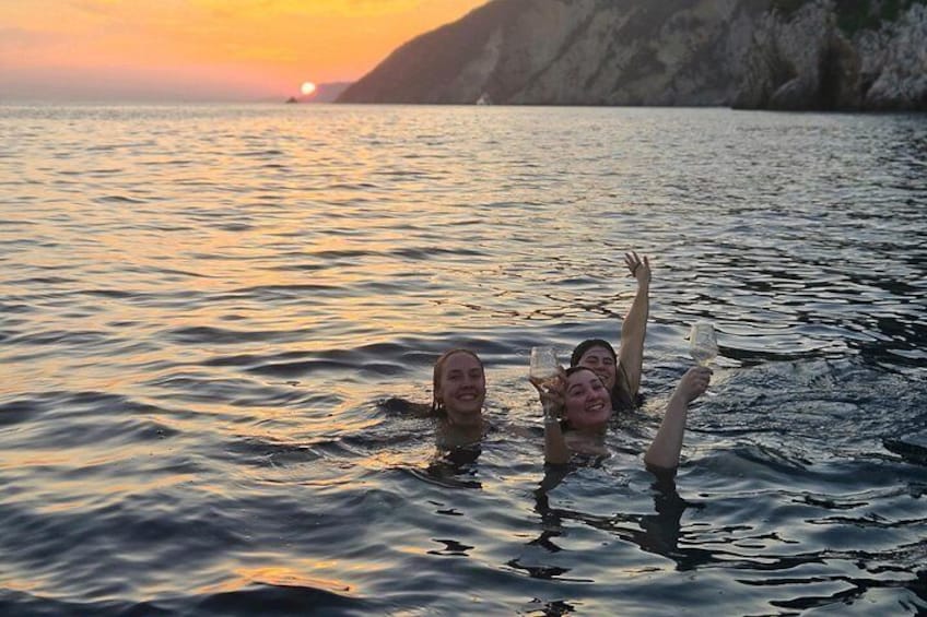Twee mensen zwemmen in het water tijdens de zonsondergang, met een bergachtig landschap op de achtergrond. 4