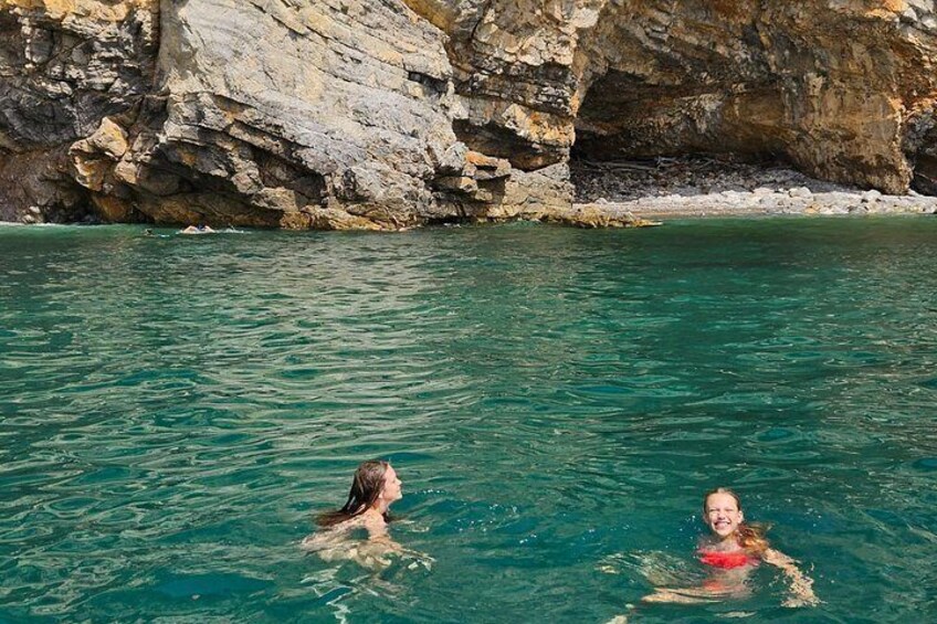 Twee mensen zwemmen in helder turquoise water, met rotsachtige kliffen op de achtergrond. 3
