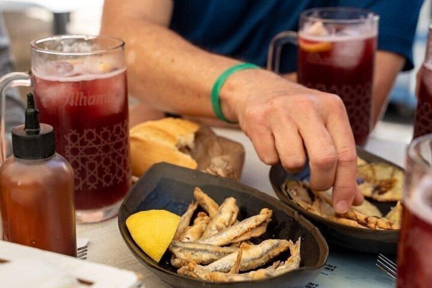 A person serving fried fish on a plate with lemon wedges, with a drink and a bottle in the background. 4