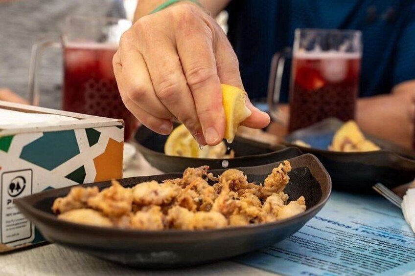 A person squeezing lemon over fried food. 3
