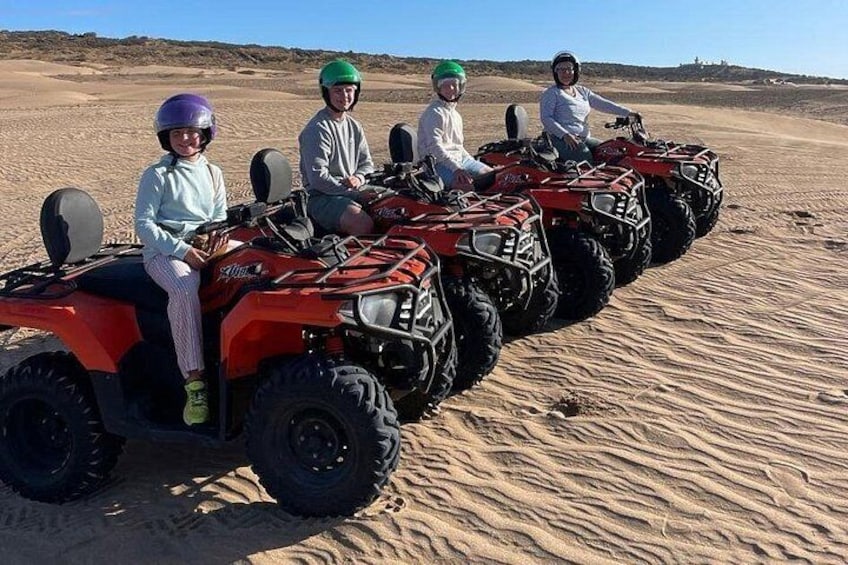 Four people on ATVs in a desert with sand dunes. 1