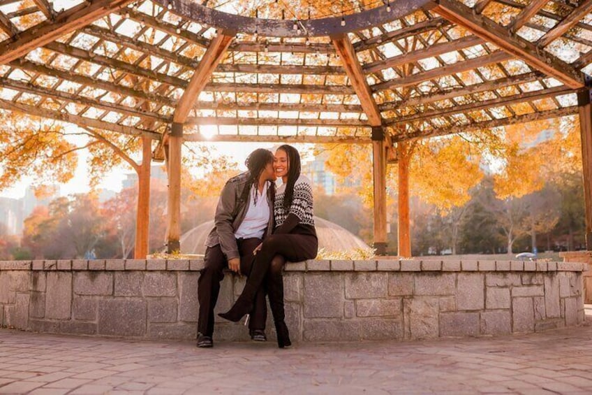 Two people sitting on a stone bench under a wooden pergola with autumn leaves in the background. 2