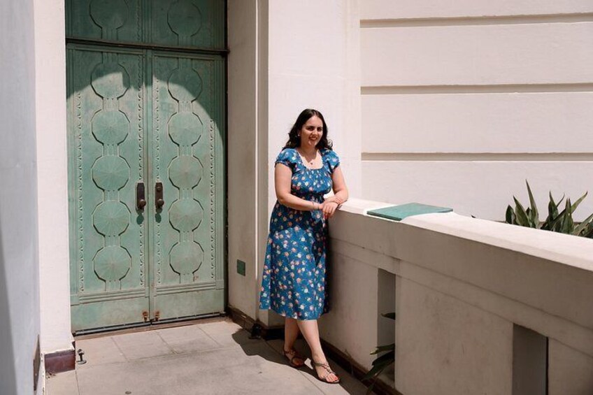 A woman in a blue dress standing on a balcony with a green door in the background. 3