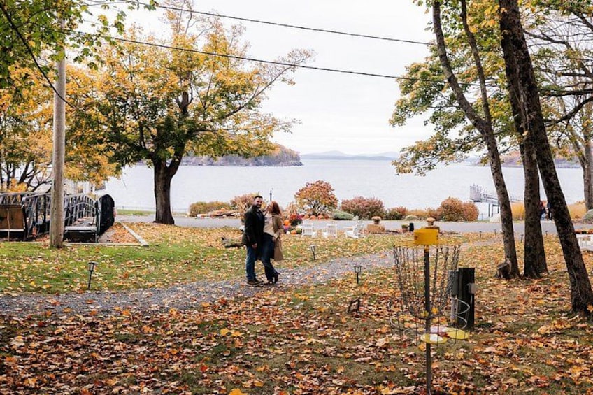 A couple walking along a path by a lake with autumn leaves on the ground. 2