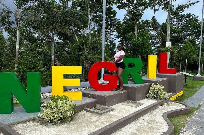 A person standing on a platform with large letters spelling 'NEGRIL' in green, yellow, and red. 2