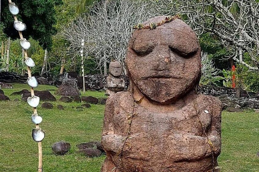 A stone statue with a face, surrounded by rocks and greenery. 1